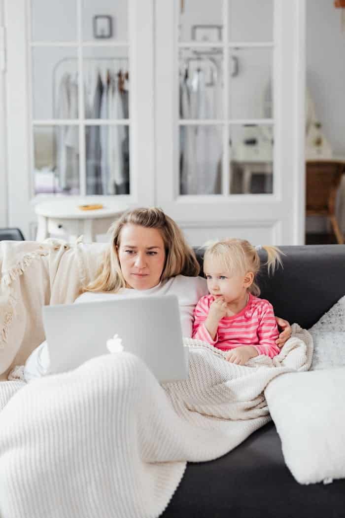 A mother and daughter cozy up on the sofa, sharing a laptop in a home setting, enjoying quality bonding time.
